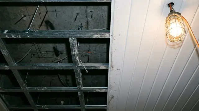 Estrutura metálica de forro vista de baixo, com os perfis cruzando o vão e um trecho já fechado por réguas de PVC.