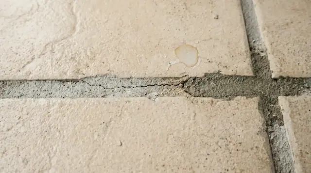 Detalhe de uma junta de rejunte entre peças de porcelanato, com trecho escurecido, trinca fina no meio e diferença de tom entre os lados.